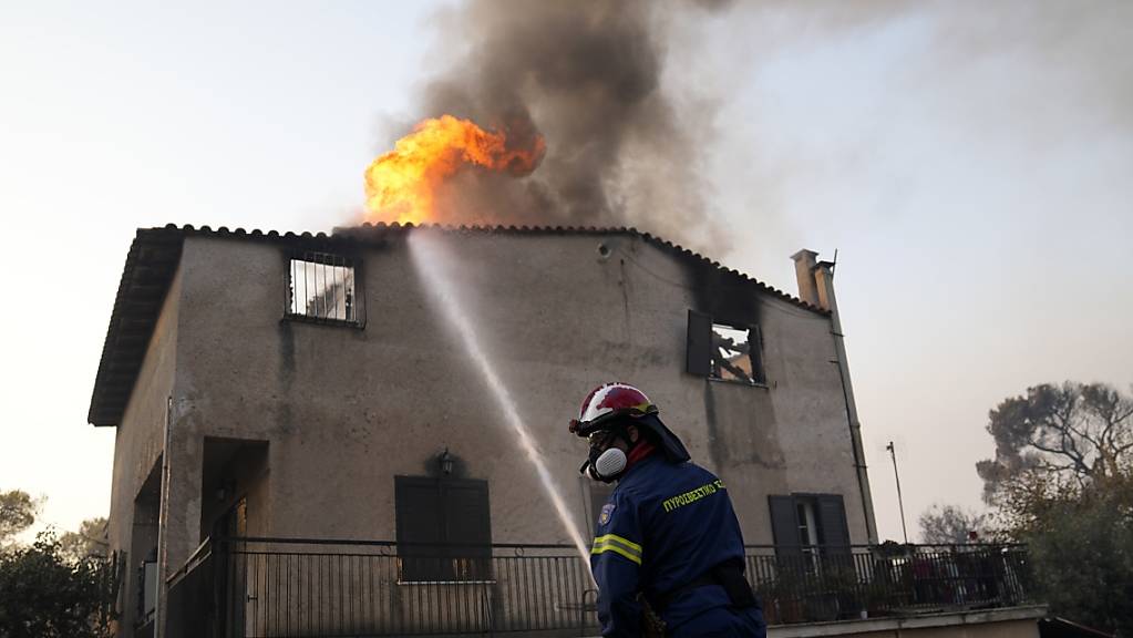 Ein Feuerwehrmann löscht einen Brand an einem Gebäude, der durch das Feuer von Waldbrände entfacht ist. Feuerwehrleute in Griechenland kämpfen auch am Mittwochmorgen weiter gegen den Großbrand in den nördlichen Vorstädten Athens. Regierungschef Kyriakos Mitsotakis sprach von einem «Alptraumbrand». 