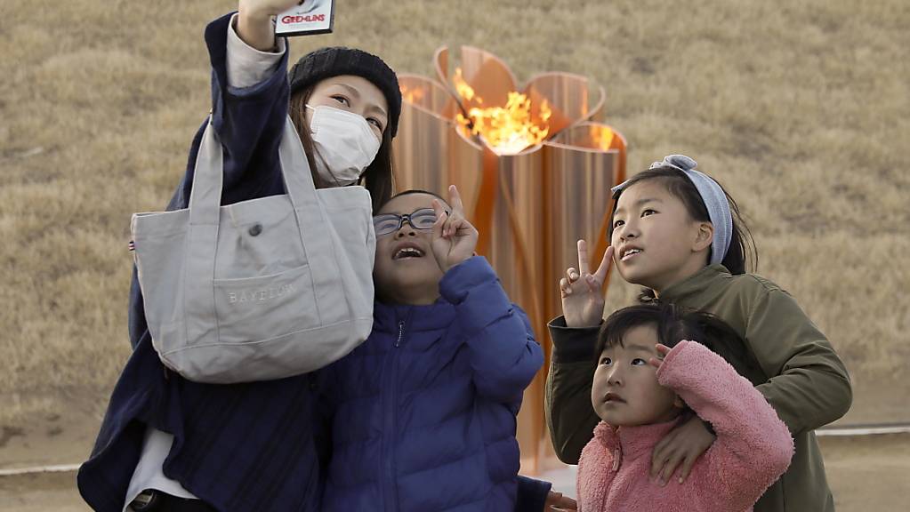 Eine Familie macht ein Selfie mit dem olympischen Feuer, das am Freitag in Japan eingetroffen ist