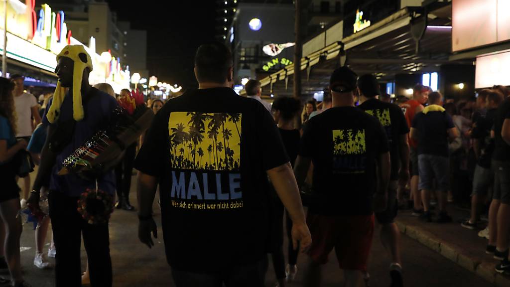 ARCHIV - Männer, die ein T-Shirt mit der Aufschrift «Malle» tragen, gehen durch die Schinkenstraße im so genannten Ballermann-Viertel auf Mallorca. Foto: Clara Margais/dpa