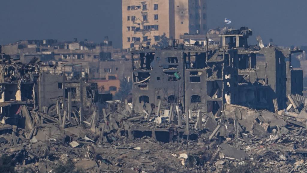 Eine israelische Fahne weht auf einem Dach eines zerstörten Gebäudes im Gazastreifen, vom Süden Israels aus gesehen. Foto: Ariel Schalit/AP/dpa