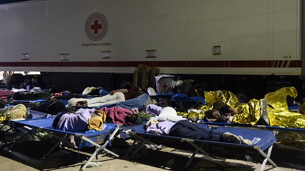 Migranten schlafen vor dem Aufnahmezentrum für Migranten. Der Stadtrat der italienischen Mittelmeerinsel Lampedusa hat angesichts Tausender neu angekommener Bootsmigranten den Notstand ausgerufen. Foto: Valeria Ferraro/AP/dpa