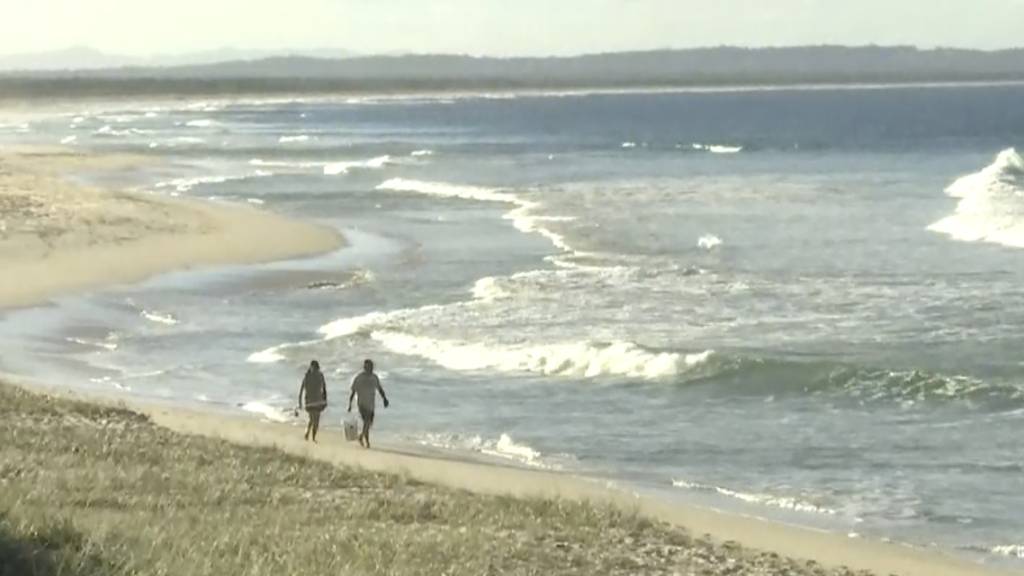 In diesem Standbild aus einem Video gehen Menschen an einem Strand in Tuncurry, Australien entlang.