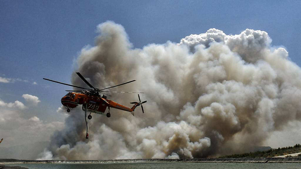 Ein Löschhubschrauber fliegt während eines Waldbrandes über einen Wasserspeichertank. Foto: Valerie Gache/AP/dpa