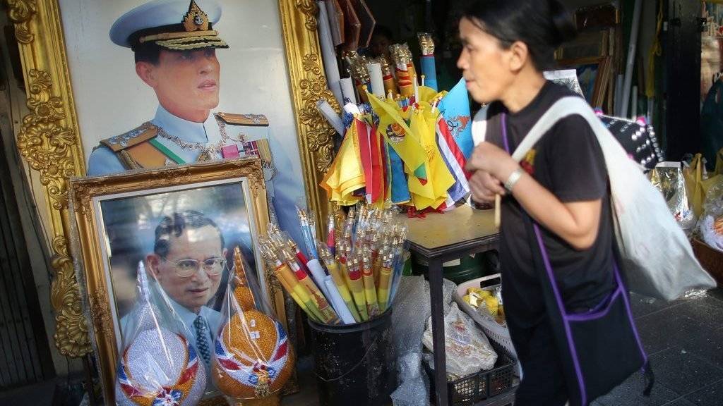 Ein Frau läuft in der thailändischen Hauptstadt Bangkok an den Porträts des verstorbenen Königs Bhumibol Adulyadej (unten) und des Kronprinzen Maha Vajiralongkorn (oben) vorbei. Letzterer will die Nachfolge seines Vaters frühestens in einem Jahr antreten.