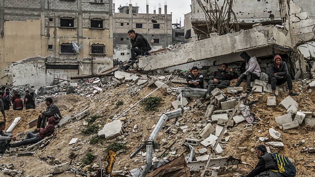 Menschen sitzen auf den Ruinen von Gebäuden, die durch israelische Luftangriffe zerstört wurden. Foto: Mahmoud Issa/dpa