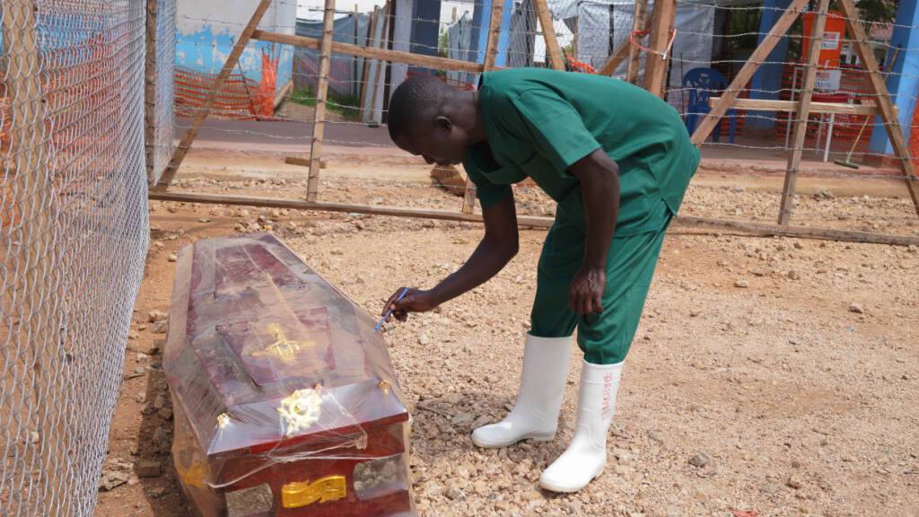 dpatopbilder - Ein Mitarbeiter des Bestattungsteams beschriftet im Behandlungszentrum des Allgemeinen Krankenhauses im Osten des Kongo einen Sarg. Knapp drei Monate nach Bekanntgabe des Ebola-Ausbruchs im Kongo sind bereits mehr als 2.000 Menschen gestorben. Foto: Dieudonne Dirole/AP/dpa