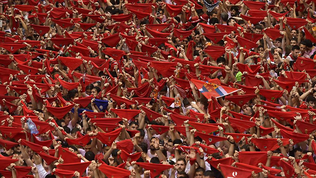 Feiernde halten rote Tücher in die Höhe, während sie den Hauptplatz zu Beginn der neuntägigen, ununterbrochenen Feierlichkeiten des berühmten Bullenlauf-Festivals bevölkern. Foto: Alvaro Barrientos/AP/dpa