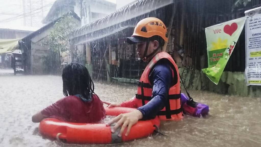 HANDOUT - Dieses von der philippinischen Küstenwache zur Verfügung gestellte Foto zeigt eine Rettungskraft die ein Mädchen durch das Hochwasser evakuiert. Foto: Uncredited/Philippine Coast Guard/dpa - ACHTUNG: Nur zur redaktionellen Verwendung und nur mit vollständiger Nennung des vorstehenden Credits