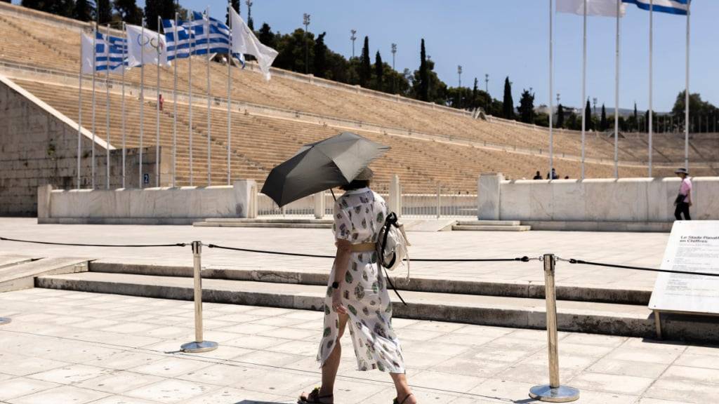 ARCHIV - Eine Touristin mit Schirm vor dem Panathinaiko-Stadion in Athen. Foto: Socrates Baltagiannis/dpa/Archivbild
