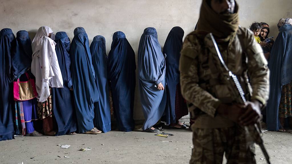 ARCHIV - Ein Taliban-Kämpfer steht Wache, während Frauen darauf warten, von einer humanitären Hilfsorganisation verteilte Lebensmittelrationen zu erhalten. Foto: Ebrahim Noroozi/AP/dpa