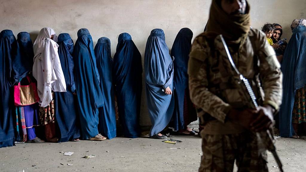 ARCHIV - Ein Taliban-Kämpfer steht Wache, während Frauen darauf warten, von einer humanitären Hilfsorganisation verteilte Lebensmittelrationen zu erhalten. Foto: Ebrahim Noroozi/AP/dpa