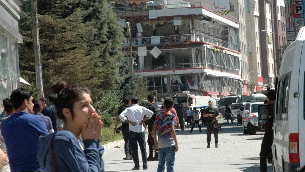 Passanten und Sicherheitskräfte stehen vor dem Provinzbüro der türkischen Regierungspartei AKP in der Stadt Van, das bei einem Autobombenanschlag stark beschädigt wurde.