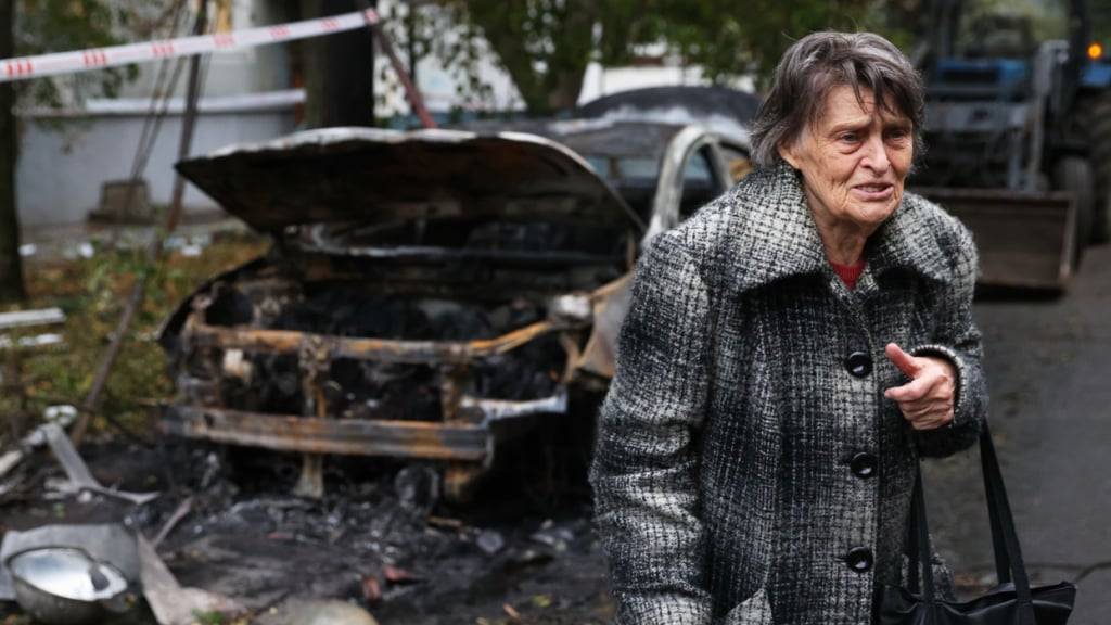 dpatopbilder - Eine ältere Frau neben einem zerstörten Auto in Saporischschja. Foto: Kateryna Klochko/AP/dpa