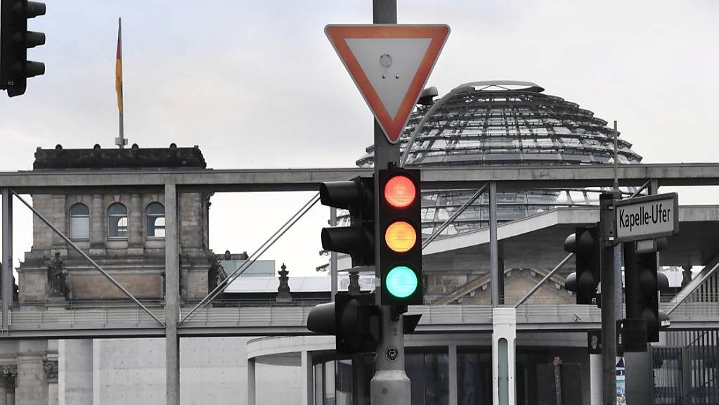 ARCHIV - Eine Ampel, an der die Farben Rot, Gelb und Grün gleichzeitig leuchten, ist vor der Kuppel des Reichstagsgebäudes zu sehen. SPD, Grüne und FDP wollen über eine mögliche Ampelkoalition verhandeln. Foto: Julian Stratenschulte/dpa