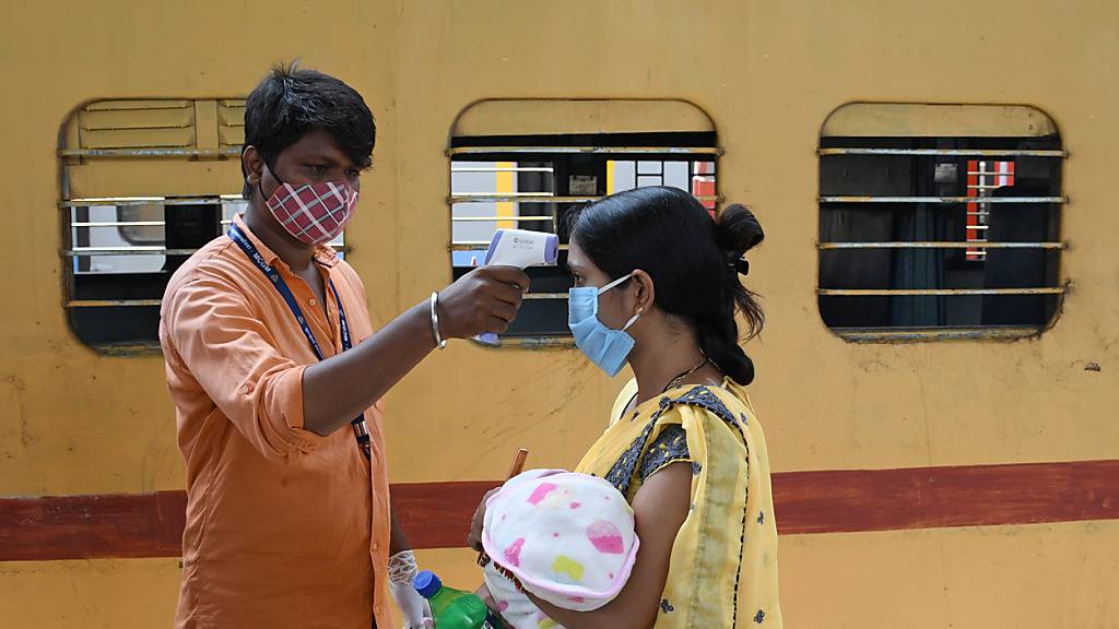 Ein Mitarbeiter misst die Temperatur bei einer Frau, die ein Baby auf dem Arm trägt, auf einem Bahnsteig im indischen Mumbai. Foto: Ashish Vaishnav/SOPA Images via ZUMA Wire/dpa