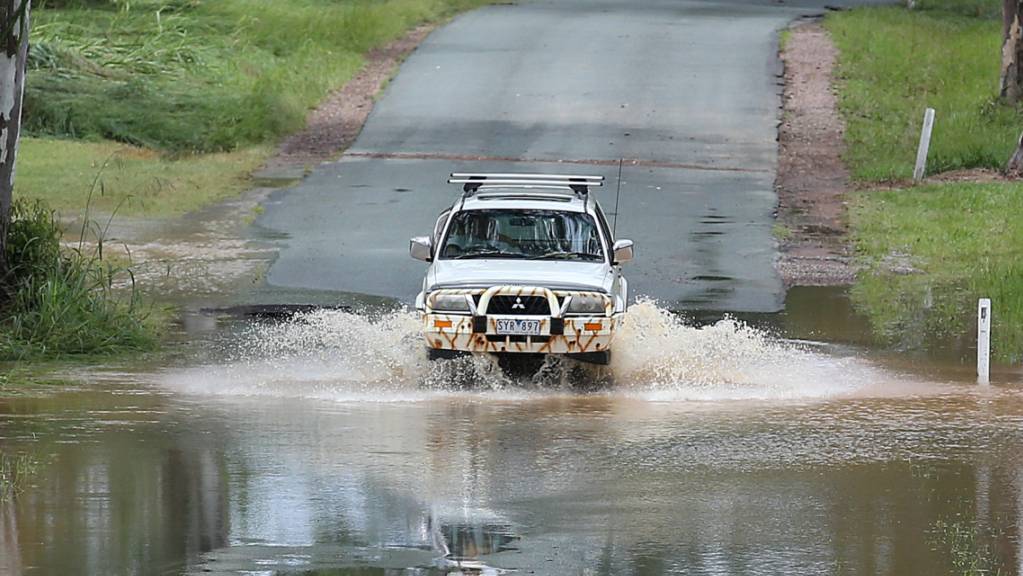 A car crosses flood waters near Belli Creek, on the Sunshine Coast, Queensland, Wednesday, February 23, 2022. The body of a 60-year-old has been found in a submerged car in a creek on Queensland's Sunshine Coast after severe rainfall triggered flash floods. (AAP Image/Jono Searle) NO ARCHIVING