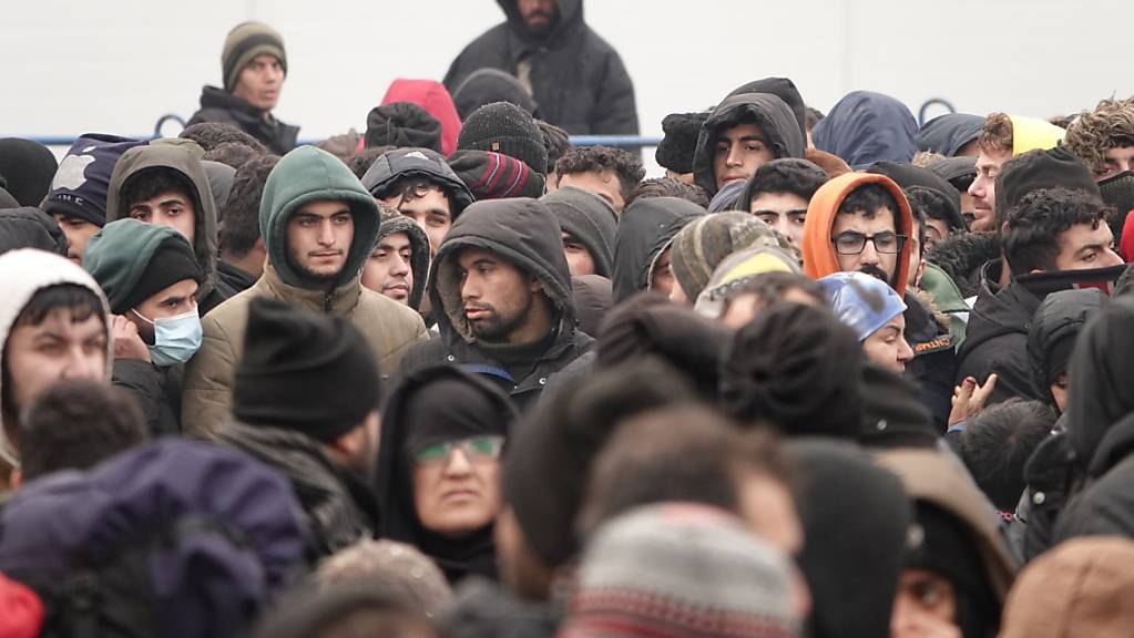 Migranten warten vor einer Lagerhalle in der Nähe der Grenze, die als Notunterkunft eingerichtet wurde. Foto: Ulf Mauder/dpa