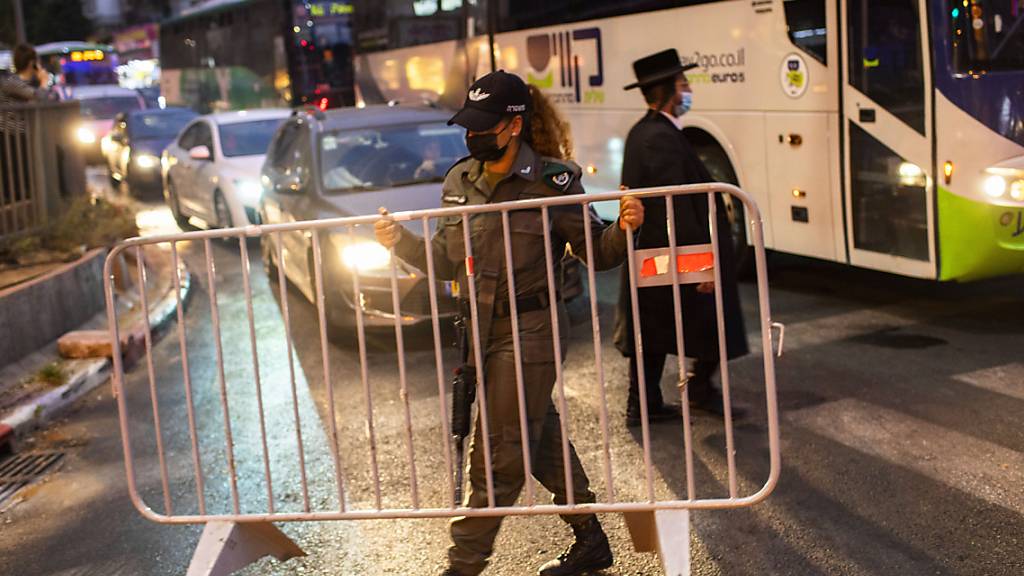 dpatopbilder - Ein israelischer Grenzpolizist errichtet in der ultra-orthodoxen jüdischen Stadt Bnei Brak vor einer nächtlichen Ausgangssperre auf einer Hauptstraße eine Absperrung. Foto: Oded Balilty/AP/dpa