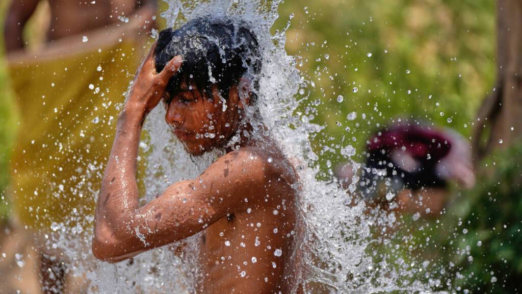 ARCHIV - Ein Junge kühlt sich in der großen Sommerhitze an einem Wasserhahn auf einer Straße in Indien ab. Foto: Channi Anand/AP/dpa/Archivbild