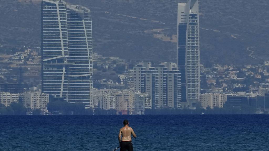 ARCHIV - Ein Mann steht auf einem Paddleboard im Meer vor der Aussicht auf die Hochhäuser in der Küstenstadt Limassol. Foto: Petros Karadjias/AP/dpa