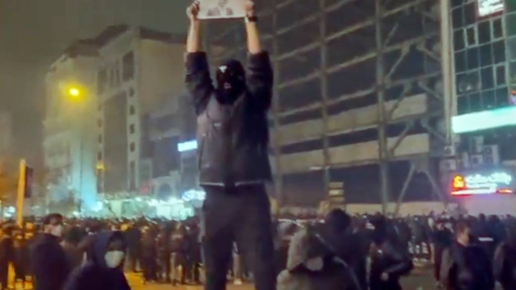 SCREENSHOT - In diesem Bild aus einem Video, das die Nachrichtenagentur AP außerhalb des Irans erhalten hat, hält ein maskierter Demonstrant ein Bild des iranischen Kronprinzen Reza Pahlavi während einer Demonstration in Teheran. Foto: Uncredited/UGC via AP/dpa - ACHTUNG: Nur zur redaktionellen Verwendung im Zusammenhang mit der aktuellen Berichterstattung und nur mit vollständiger Nennung des vorstehenden Credits