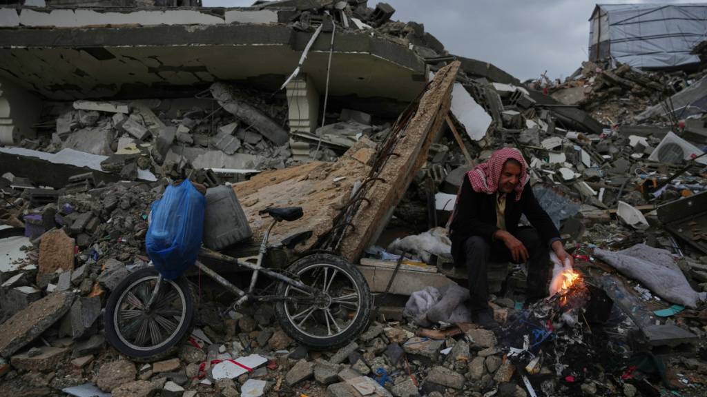 dpatopbilder - Der Palästinenser Mohammed al-Jabri, 58, wärmt sich neben dem Feuer, während er auf den Trümmern eines Gebäudes sitzt, das während der israelischen Luft- und Bodenoperationen im Viertel Sheikh Radwan zerstört wurden. Foto: Abdel Kareem Hana/AP/dpa