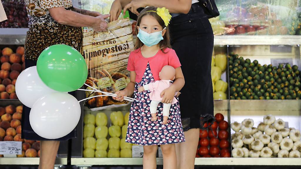 Ein Mädchen mit medizinischem Mundschutz hält Luftballons und eine Puppe in einem Lebensmittelmarkt in Bukarest. Rumänien verzeichnet einen Rekord an Neuinfektionen mit dem Coronavirus.