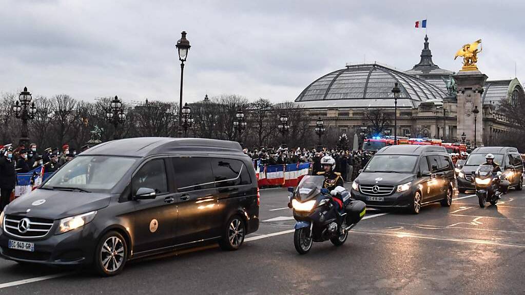 Fahrzeuge mit den Särgen von drei französischen Soldaten fahren in Paris über die Brücke Alexandre III an einer Gruppe von Menschen vorbei, die den Soldaten gedenken. Foto: Alain Jocard/AFP/dpa