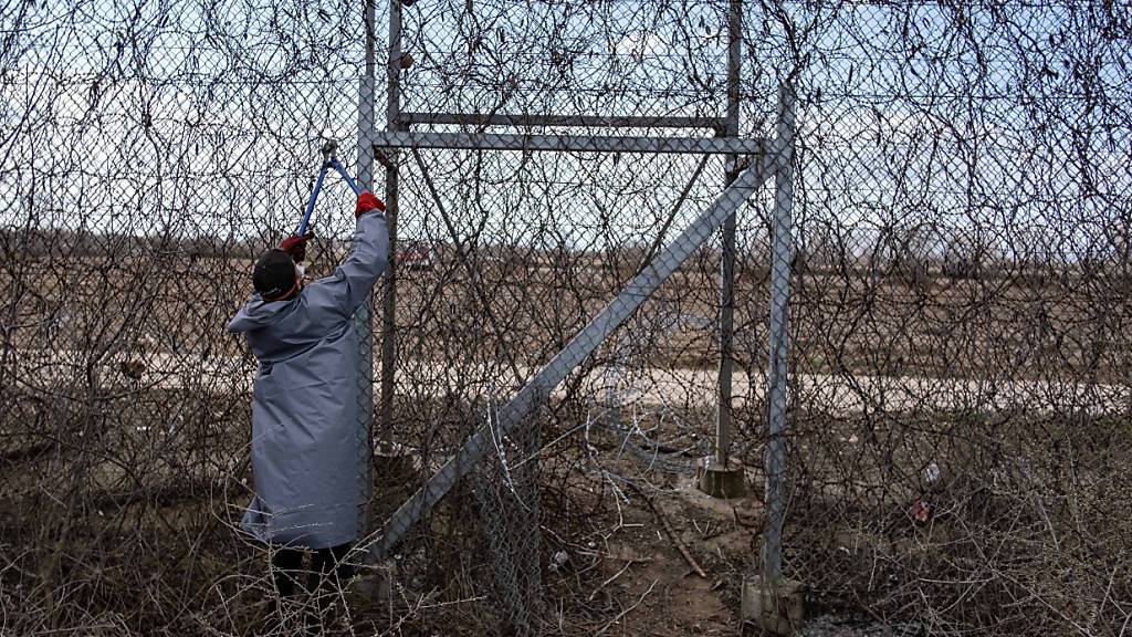 Ein Migrant steht am Grenzzaun an der türkisch-griechischen Grenze und versucht, mit einer Drahtschere den Zaun durchzuschneiden.