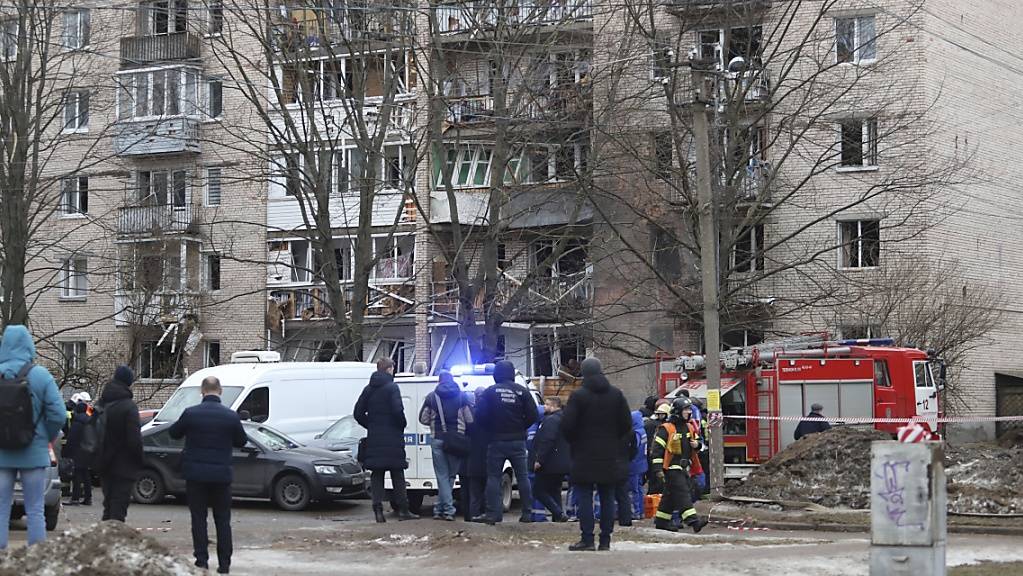 Menschen beobachten, wie Rettungskräfte nach einer Explosion an der Seite des beschädigten Wohnhauses in Sankt Petersburg arbeiten.