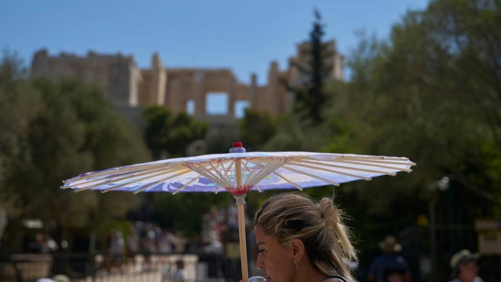 ARCHIV - Eine Touristin mit einem Sonnenschirm steht auf der Akropolis. Foto: Petros Giannakouris/AP/dpa/Archiv