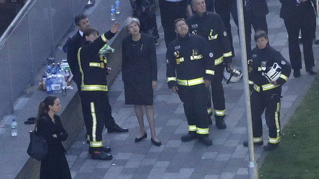 Brandursache ungeklärt: Premierministerin May sichtet gemeinsam mit Feuerwehrleuten das ausgebrannte Gebäude.