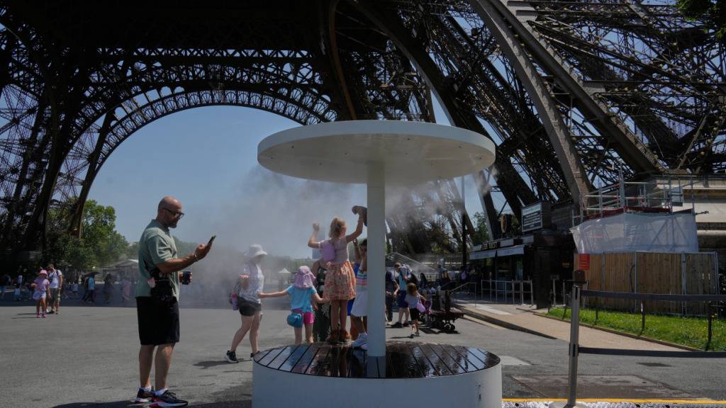 ARCHIV - Menschen erfrischen sich am Eiffelturm unter einem Wassersprühnebel. Foto: Michel Euler/AP/dpa