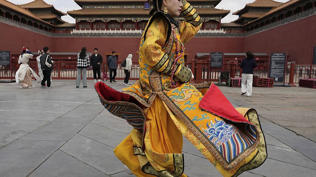 Eine Frau im Gewand einer Kaiser-Witwe schützt ihr Outfit vor dem starken Wind vor der Verbotenen Stadt, die wegen Sturmwarnungen geschlossen wurde. Foto: Ng Han Guan/AP/dpa