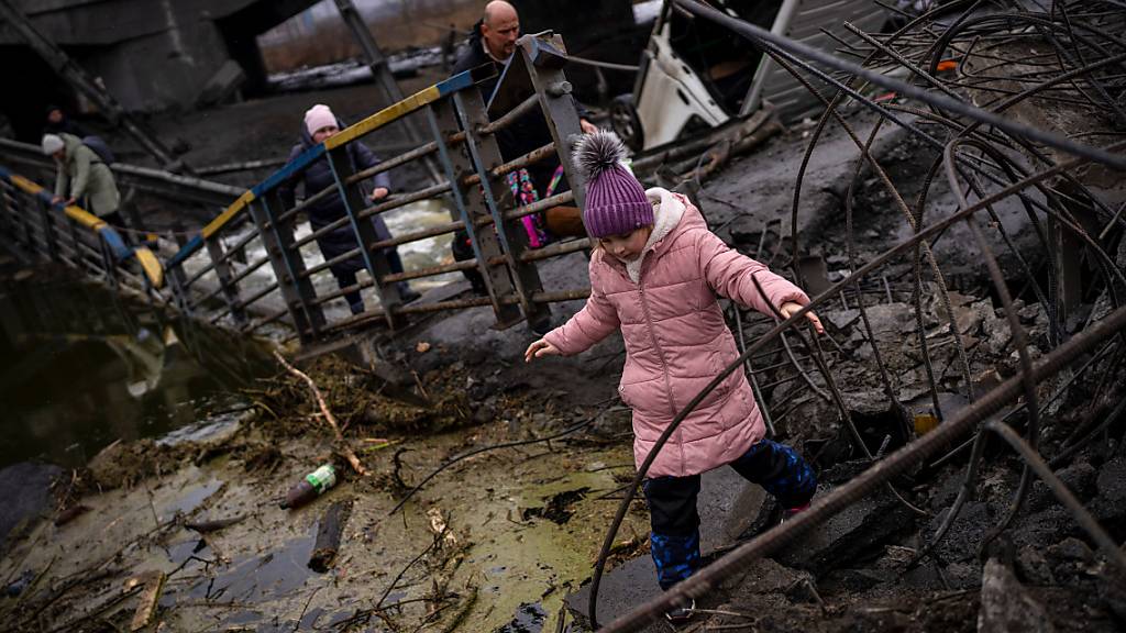 Ein Mädchen flieht mit seiner Familie über eine zerstörte Brücke am Rande von Kiew. Die russischen Streitkräfte haben ihre Angriffe auf belebte Städte ausgeweitet, was der ukrainische Staatschef als unverhohlene Terrorkampagne bezeichnet. Foto: Emilio Morenatti/AP/dpa