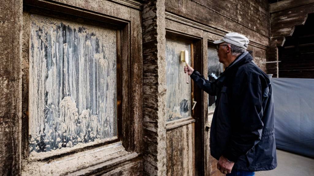 Ein Anwohner, Arnold Rubin, entfernt den Schmutz an der Fassade seines Chalets mit einer Bürste.