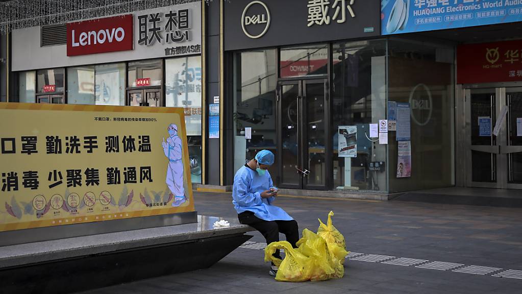 Ein Mann mit Maske surft auf seinem Smartphone, während er sich auf einer Bank mit einem Plakat zur Corona-Prävention in der Nähe der geschlossenen Geschäfte im Huaqiangbei-Gebiet, dem grössten Elektronikmarkt der Welt, in Shenzhen in der südchinesischen Provinz Guangdong ausruht. 