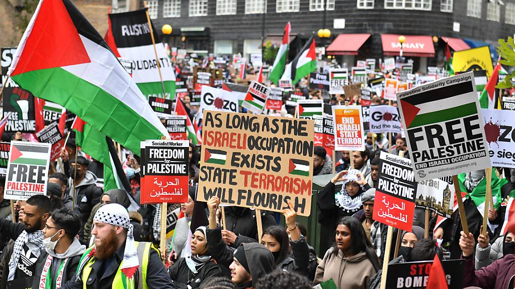 Demonstranten halten Plakate und palästinensische Flaggen während eines Protests in London. Tausende Menschen haben in der britischen Hauptstadt gegen die Luftangriffe der israelischen Armee auf Gaza demonstriert. Foto: Dominic Lipinski/PA Wire/dpa