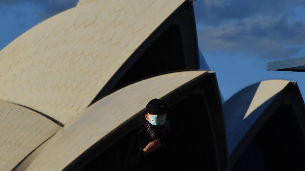 A pedestrian wearing a mask walks past the Sydney Opera House in Sydney, Saturday, June 26, 2021. All of greater Sydney, the Central Coast, the Blue Mountains and Wollongong regions will enter a two-week coronavirus lockdown until 9 July and new restrictions will be in place for the remainder of New South Wales. (AAP Image/Mick Tsikas) NO ARCHIVING
