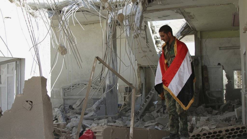 Ein Mann mit einer syrischen Flagge um die Schultern steht in einem zerstörten Haus in der Provinz Hama.
