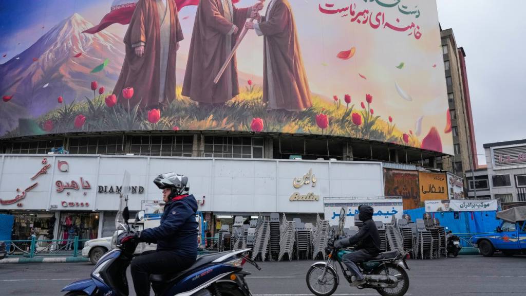 dpatopbilder - Fahrzeuge fahren an einer Plakatwand vorbei, die den verstorbenen iranischen Obersten Führer Ajatollah Ali Chamenei, Mitte, zeigt, wie er die Flagge des Landes an seinen Sohn und Nachfolger Ayatollah Mojtaba Chamenei, rechts, übergibt. Foto: Vahid Salemi/AP/dpa