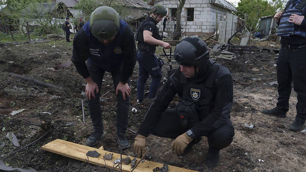 Ein ukrainischer Polizeibeamter und ein Staatsanwalt für Kriegsverbrechen inspizieren Bruchstücke einer Gleitbombe vor einem beschädigten Haus nach einem russischen Luftangriff auf ein Wohnviertel. Foto: Evgeniy Maloletka/AP/dpa