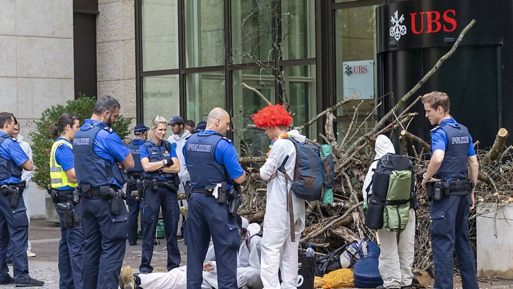Polizisten räumten am Montag die Blockade der Aktivisten einer Gruppe namens «Collective Climate Justice» vor dem UBS-Bürogebäude am Aeschenplatz in Basel. Im Hintergrund eine Holzbeige, die an Schwemmholz erinnert, als Sperre vor der Türe. (Archivbild)