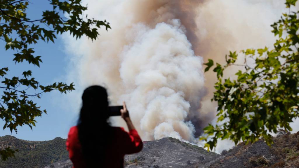 Eine Frau fotografiert den Rauch eines Waldbrandes in Simi Valley. Foto: Caroline Brehman/FR172323 AP/AP/dpa