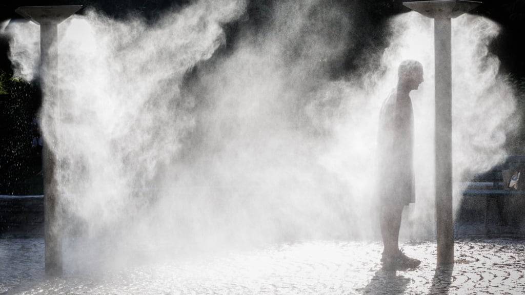 ARCHIV - Ein Mann steht an einem heißen Tag unter einem Wasserzerstäuber in Saint Ouen. Foto: Sadak Souici/ZUMA Press Wire/dpa/Archivbild