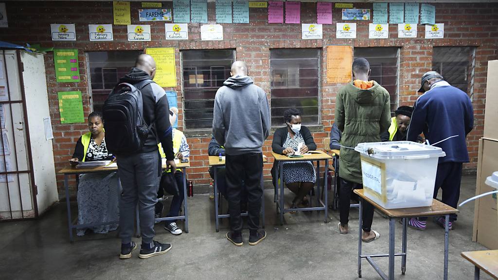 Menschen nehmen ihre Wahlunterlagen während der Präsidenten- und Parlamentswahl in einem Wahllokal entgegen, nachdem die Wahlen um einen Tag verlängert wurden. Foto: Tsvangirayi Mukwazhi/AP/dpa