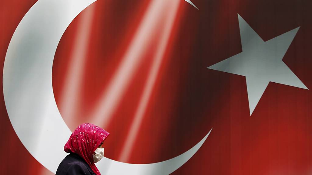 ARCHIV - Eine Frau, die eine Maske trägt, geht in Istanbul an einer türkischen Flagge vorbei.(Symbolbild) Foto: Emrah Gurel/AP/dpa