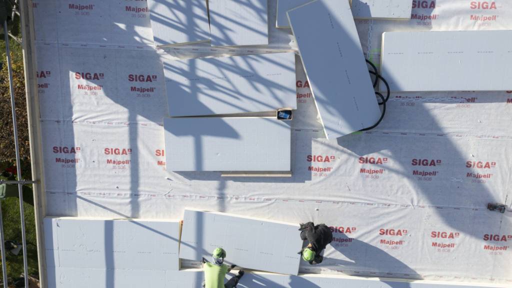 Bauarbeiter tragen und verteilen Isolierplatten auf dem Dach: Die Modernisierung der Dachdämmung trägt zur energetischen Sanierung eines Gebäudes bei und somit auch zur Reduktion von Treibhausgasen.