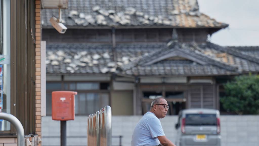 Eine Person sitzt in der Nähe eines durch ein Erdbeben beschädigten Hauses in der Präfektur Kumamoto. Foto: Hiro Komae/AP/dpa