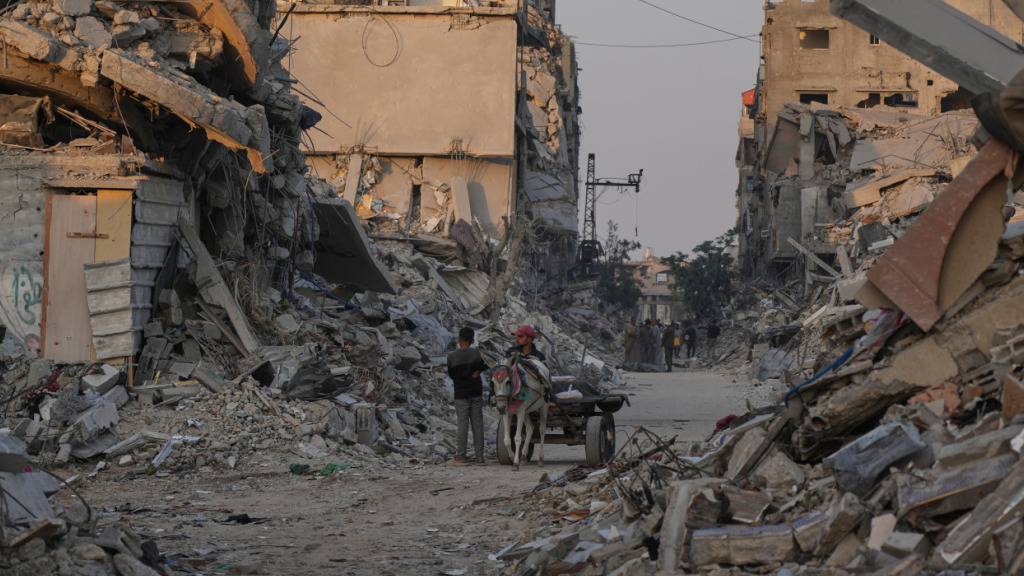 Palästinenser gehen an Häusern vorbei, die durch die israelische Luft- und Bodenoffensive zerstört wurden. Foto: Abdel Kareem Hana/AP/dpa/Archivbild